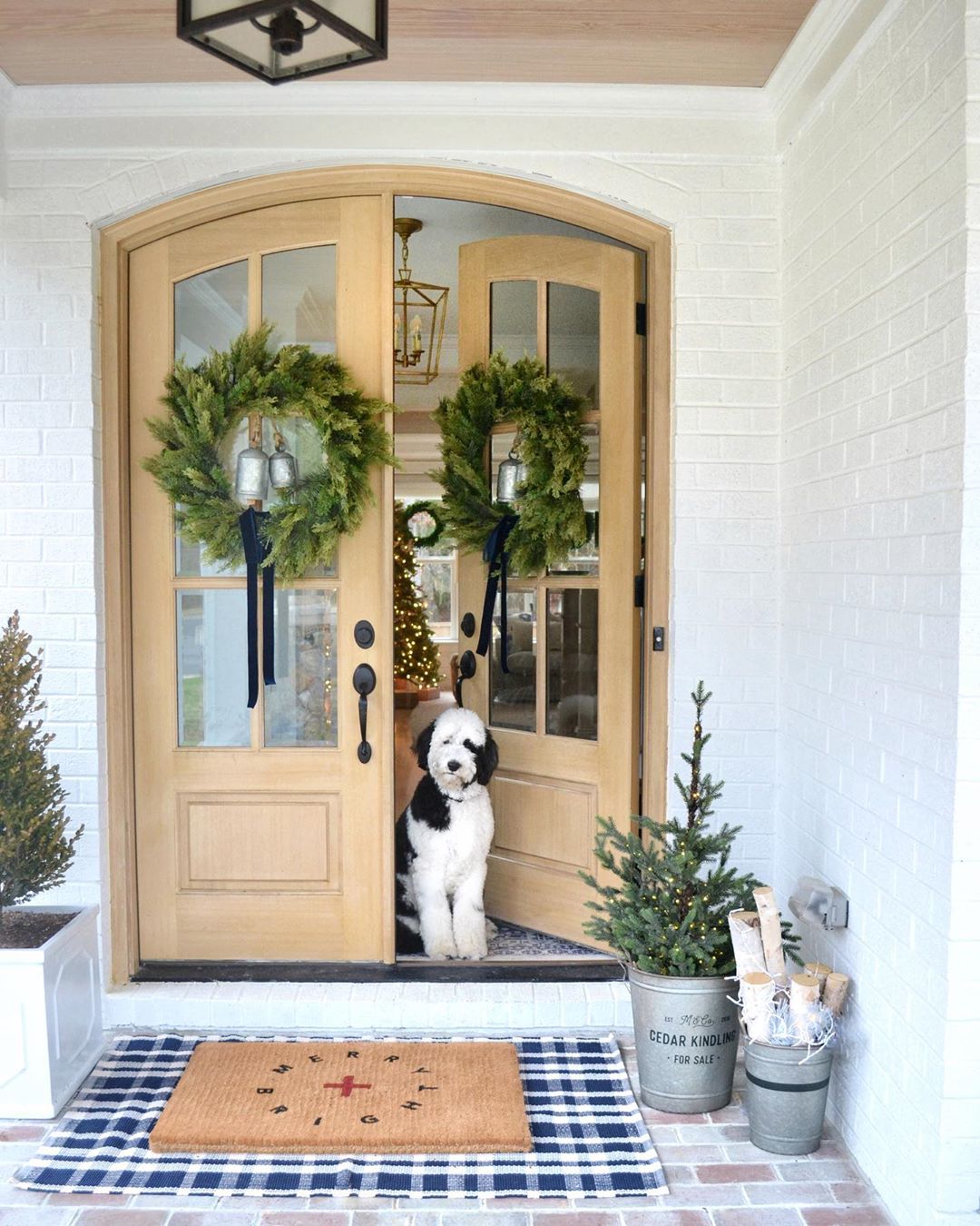 Holiday wreaths on front doors of white farmhouse with gorgeous metal roof. Charming inspiration if you love white painted house exteriors! #whitehouses #housedesign #exteriors #whitefarmhouse #holidaydecor #frontdoordecor #christmaswreaths