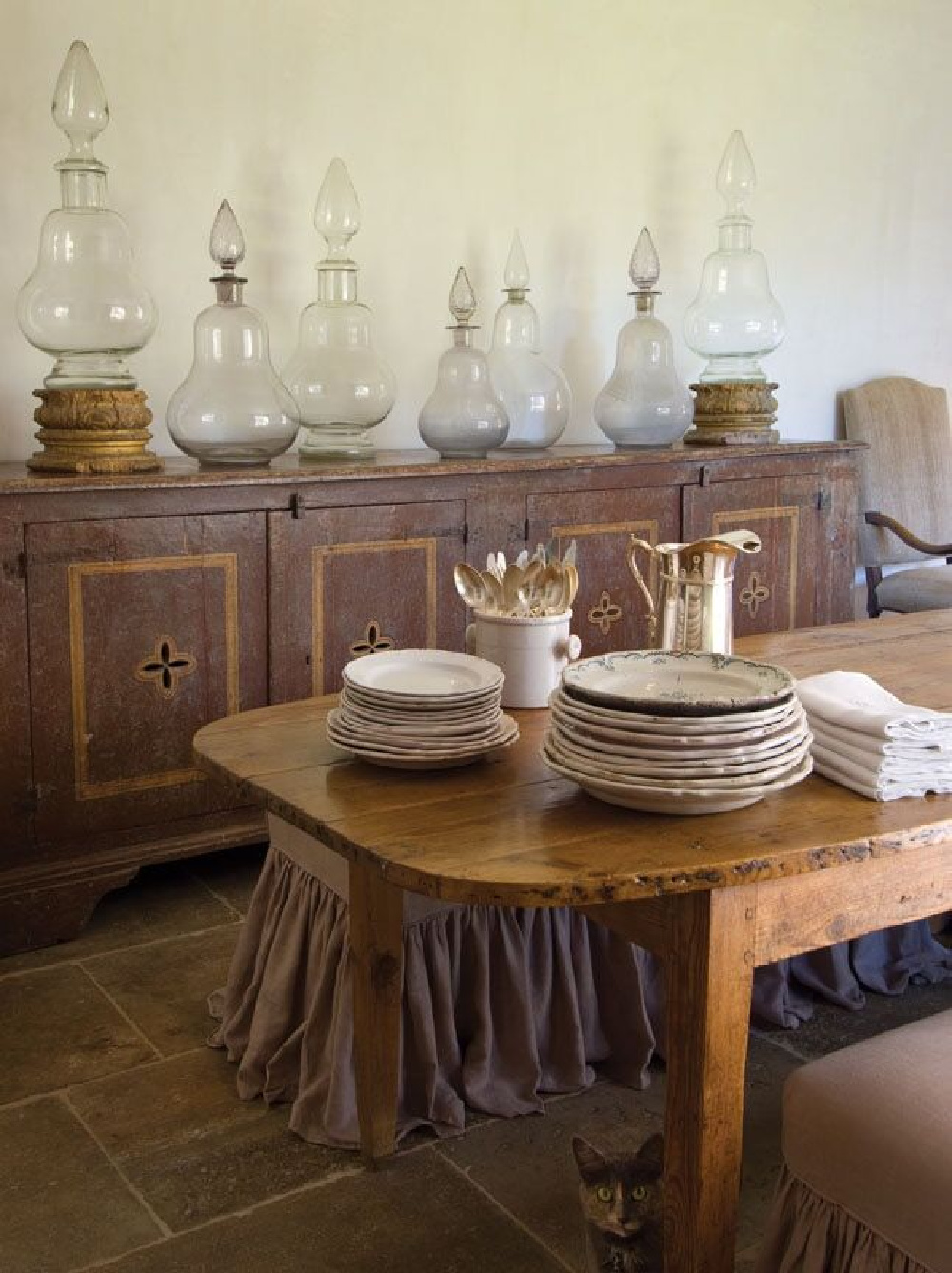 Old apothecary jars, rustic antiques from Europe, and a concerned kitty too in a dining room by Chateau Domingue. #diningrooms #interiordesign #countryfrench