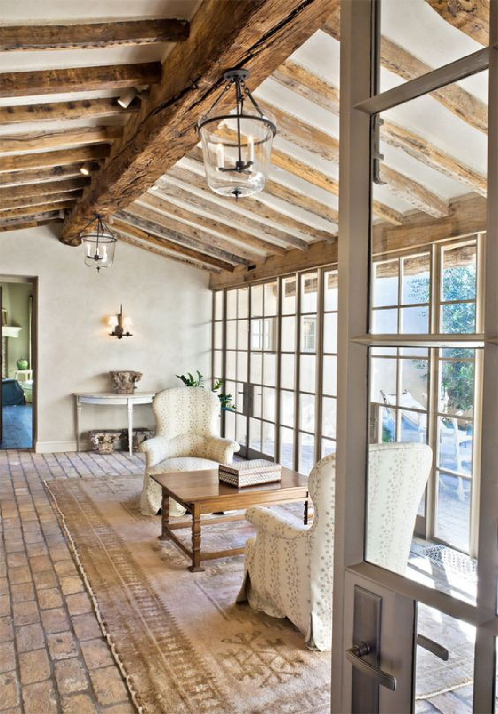 Rustic aged wood ceiling beams, brick flooring and walls of glass in a masterfully designed European country home - Oz Architects.