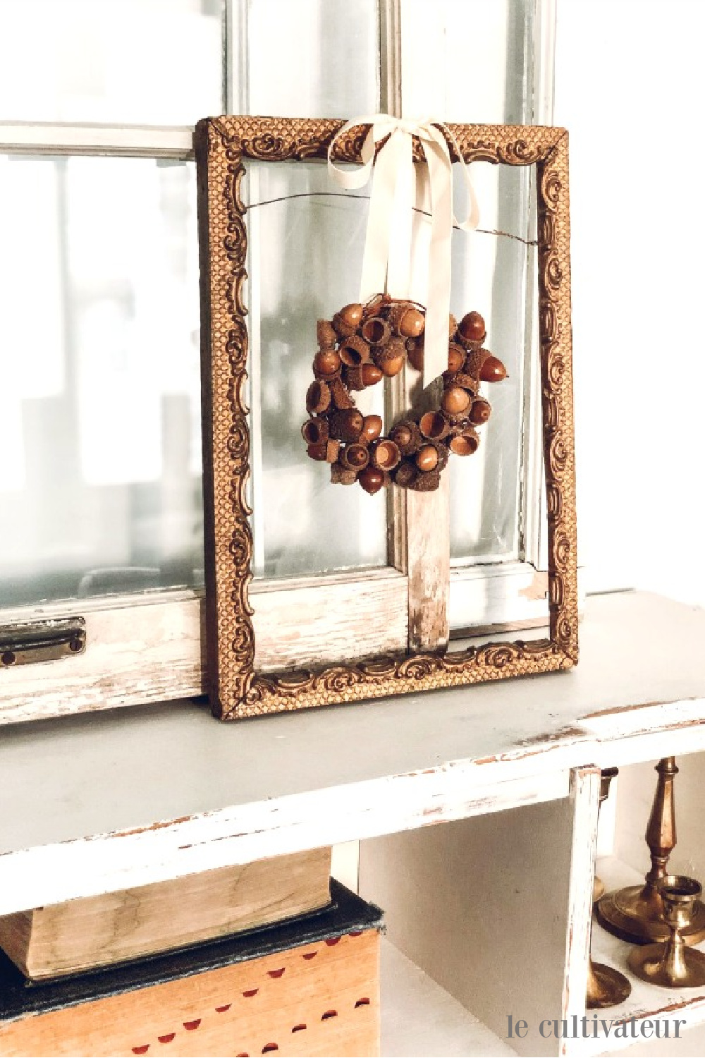 Sweet and rustic acorn wreath hangs on ribbon from vintage frame in a lovely French country white fall vignette - Le Cultivateur. #falldecor #fallwreaths #acornwreath