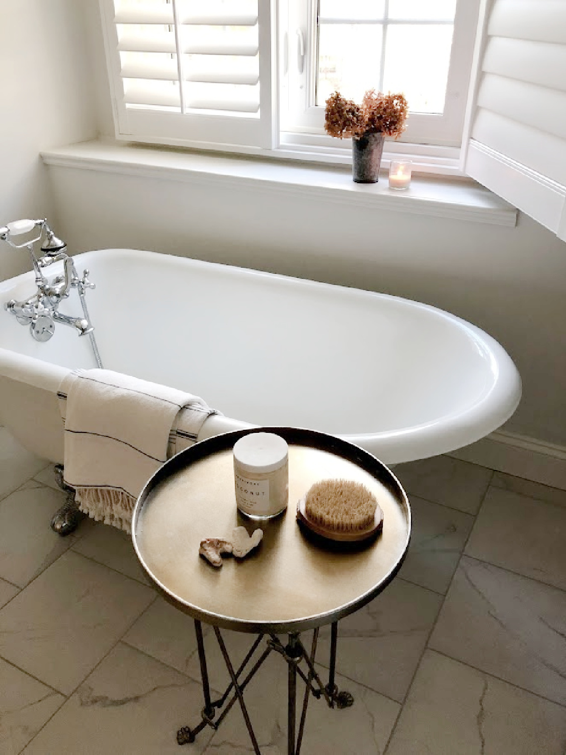 My serene bathroom with vintage clawfoot tub, Turkish towels, accent tray table, and plantation shutters - Hello Lovely Studio. #vintagebath #spalikebath #modernvintage #serenedecor
