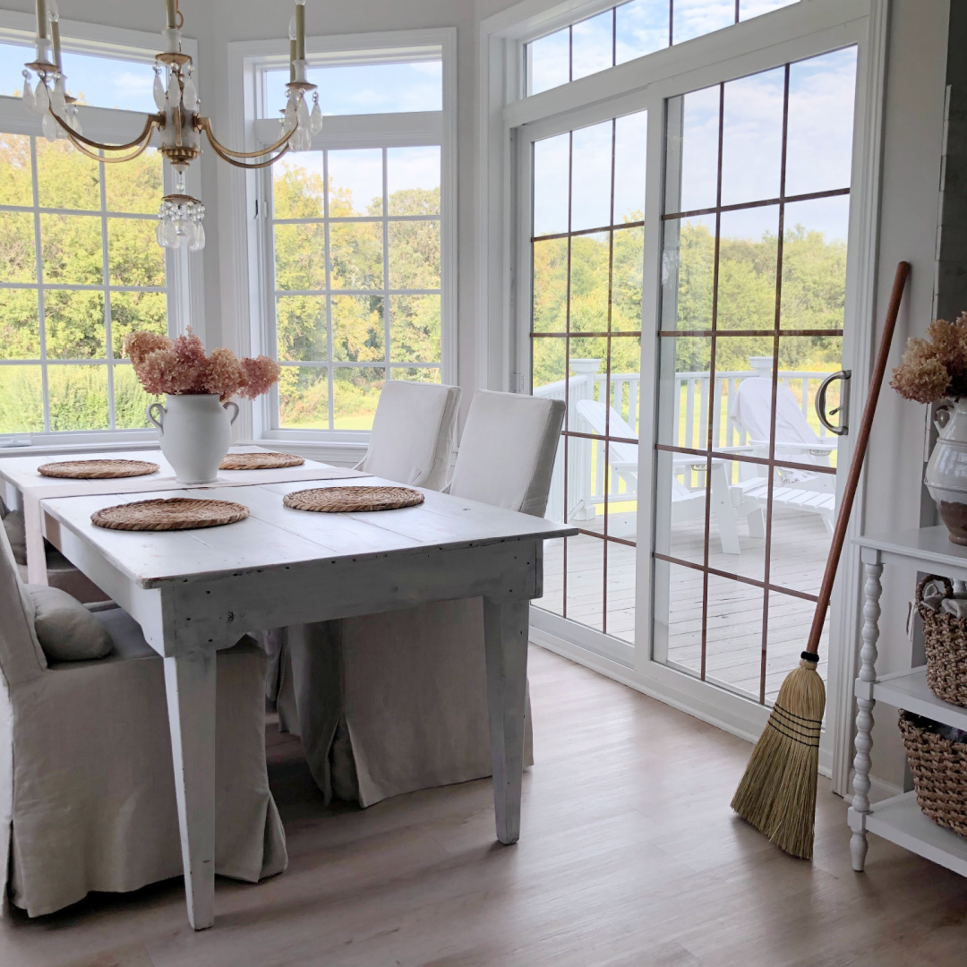 Breakfast nook with farm table, linen slipcovered chairs, handmade broom and bay window - Hello Lovely Studio.