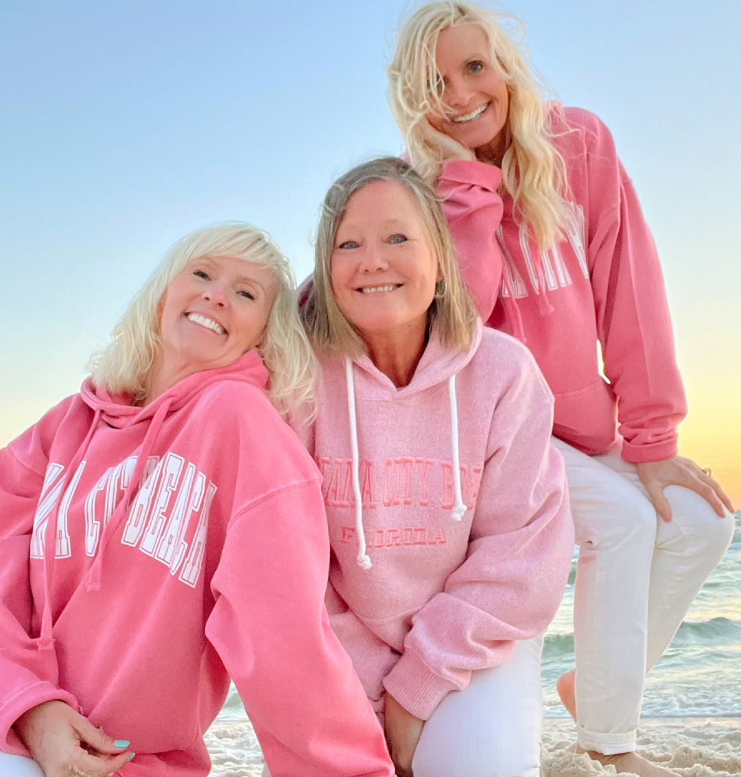 Michele and friends on beach at sunset in pink hoodies.