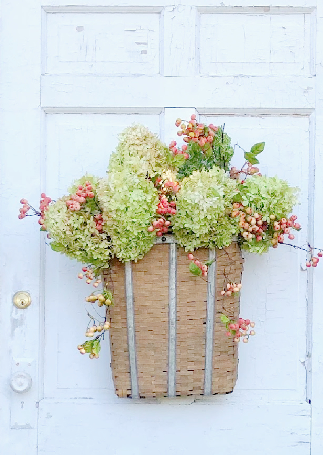 Lovely woven basket with fall floral arrangement with hydrangea and berries on a vintage white door - Hello Lovely Studio. #fallflorals #fallhydrangea #fallporch