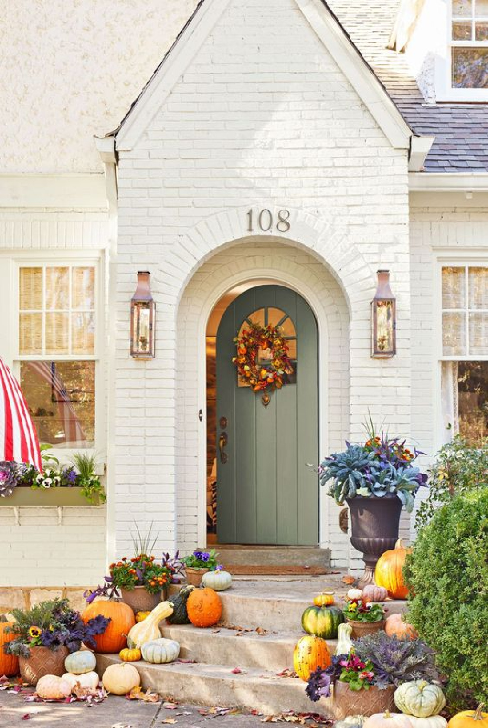 Fall porch with pumpkins, dog, planter, wreath, and arched door on white brick house - Southern Living. #falldecor #fallporch #autumnvibes